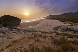 Soleil voilé, bas sur l'horizon, sur un bord de plage parsemée de gros rochers ronds.