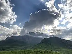 Un splendide nuage couronne une haute montagne recourverte d'herbe verte.