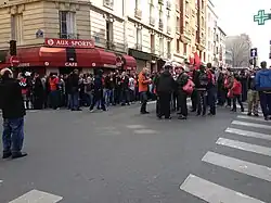 Photo montrant des personnes rassemblées dans la rue devant une enseigne rouge et noire.