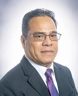 Homme en costume gris sombre à cravate violette portant de fines lunettes