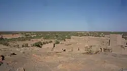 dans des tons ocres, sur trois plans, un sol de pierre, un village de terre de même couleur, et des arbres verts éparses