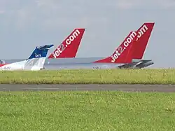 plusieurs dérives d'avion de ligne, visibles par-dessus un monticule. Chacune porte le nom d'une compagnie aérienne.