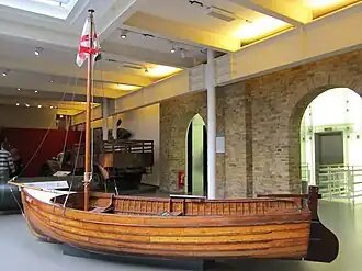 L'image présente un bateau à voile d'environ 4,5m de long posé sur le sol dans une pièce