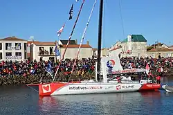 Voilier blanc et rouge, vu de profil, avançant dans le chenal des Sables-d'Olonne.
