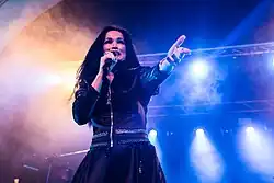 Image d'une chanteuse brune habillée d'une robe noire et tendant la main