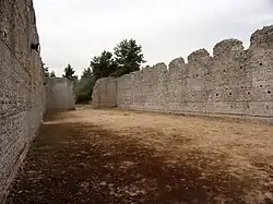 Photographie en couleurs de l'intérieur non cloisonné d'une vaste bâtiment aux murs ruinés en partie haute.