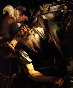 Un homme âgé, barbu et armé en position défensive tient à la main un bouclier.