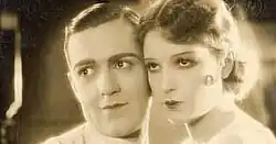 En intérieur, Fred Solm et Lili Damita, debout tête contre tête, fixent un point au loin, dans une scène du film.