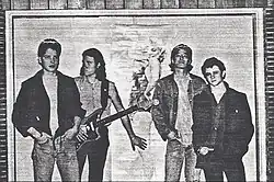 Photographie en noir et blanc de quatre hommes debout avec sur le mur un affiche de Marilyn Monroe