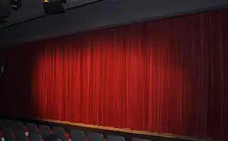  Rideau de tissu rouge formant des plis et masquant la scène.