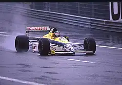 Photo d'une monoplace jaune, blanche et bleue sur une piste détrempée.