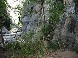 Bas de falaise avec passerelle fixée à la falaise.