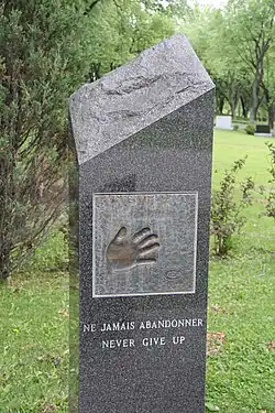 Photographie couleur de la tombe de Maurice Richard. Il y a l'empreinte d'une main ainsi que la mention en français Ne jamais abandonner puis en-dessous en anglais Never give up.
