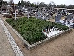 Une tombe recouverte de végétation et marquée par deux croix blanches.