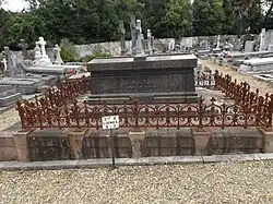 Photographie d’un tombeau entouré d’une grille dans un cimetière.