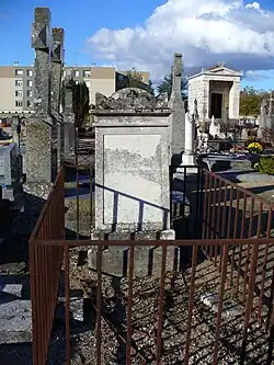 Photographie en couleurs d'une stèle funéraire de type chapelle au milieu d'un cimetière.