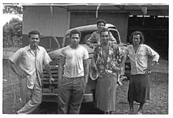 Photo en noir et blanc montrant 5 jeunes hommes polynésiens posant devant une voiture