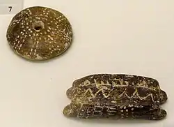 Fusaïole (en haut - décoration rappelant les lignes ambulacraires d'un test d'oursin) et navette (en bas) en terre cuite, Knossos, ~5&nbsp;800–4&nbsp;500&nbsp;ans B.C. (Néolithique). Musée archéologique d'Héraklion, Crète, Grèce