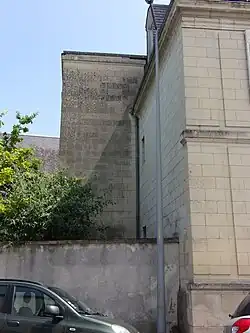 Photographie en couleurs d'une tour rectangulaire plaquée contre le pignon d'un autre bâtiment.