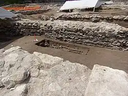 Photographie en couleurs d'un squelette dans une fosse à fleur de ferre entre deux murs dont seule reste la base.