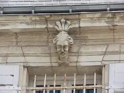 Photographie en couleurs du linteau d'une fenêtre décoré d'une sculpture de tête féminine.