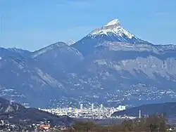 Sommet enneigé dominant des montagnes plus basses et une agglomération.