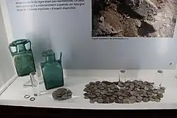 Vue de monnaies rassemblées et de deux bouteilles dans une vitrine.