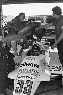Photo en noir et blanc de l'avant d'une monoplace de Formule 1, avec un pilote à l'intérieur du cockpit.