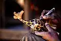 Travail à la main, finition d'une statuette Girafe en bois au village artisanal de Soumbedioune