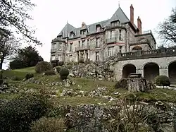 Photographie en couleurs de la façade d'un château avec un jardin de rocaille au premier plan.