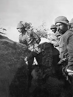 Photographie d'un groupe de soldats en uniformes légers et portant des chapeaux de feutre courant vers le sommet d'un talus la baïonnette en avant