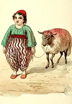 Un enfant debout habillé d'un pantalon à rayures rouges et blanches , d'un haut vert et d'un bonnet rouge tient un mouton en laisse.