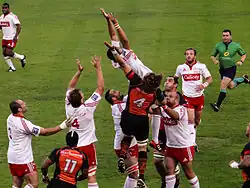 Les joueurs de deux équipes sautent afin de récupérer la retombée d'un ballon de rugby.