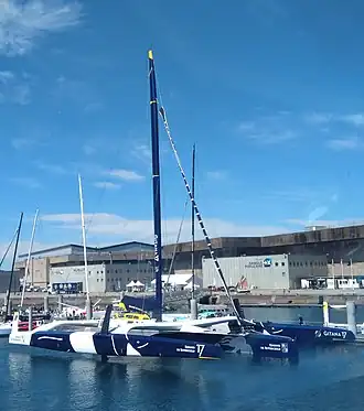 Vu en entier, de trois quarts avant, trimaran bleu et blanc amarré au ponton.