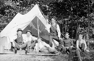 Photo noir et blanc, vers 1907 ; six hommes posent devant une toile de tente installées sous des arbres.
