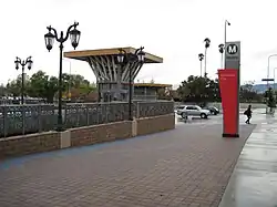 Vue de l'extérieur de l'emplacement de la station. On voit au loin les collines et des palmiers. Ciel gris.