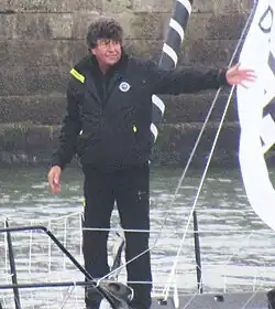 Debout à l'avant de son bateau, le navigateur, en noir, salue la foule.