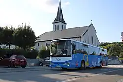 Photographie en couleurs d’un autocar blanc et bleu devant une église.