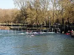 Photographie en couleurs d'un cours d'eau avec des kayaks dans les remous d'un déversoir.