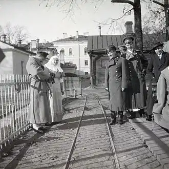 Photo en noir et blanc de six personnes en extérieur, de part et d'autre d'une voix ferrée.