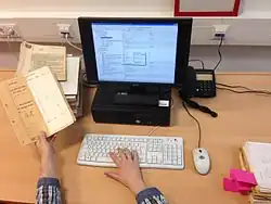 Photographie couleur de mains tenant un document d'archives et écrivant à l'ordinateur.