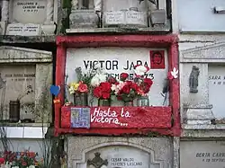 Photo d'un mur découpé en concessions, au centre une tombe peinte en rouge vif avec des fleurs