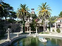 Vue extérieure vers le nord d'une partie des jardins et du bassin au premier plan. Au second plan, on distingue la villa Bianca. Orientation sud.