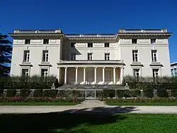 Photographie en couleurs d'un bâtiment rectangulaire à porche à colonnes.