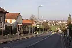 Vue d'une rue bordée de maisons descendant vers un grand espace vert ; agglomération urbaine en arrière-plan.