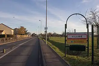 Panneau indicateur à l'entrée d'une commune ; parc de la salle des fêtes à droite ; zone résidentielle à gauche.