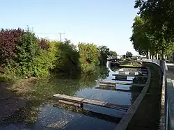 Photographie, prise depuis le quai, du canal de la Marne au Rhin et de ses pontons, avec en arrière-plan une péniche.