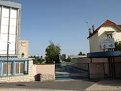 L'entrée du collège du Vieux-Port : une grille coincée entre deux bâtiments laisse apercevoir une cour de récréation et des arbres.