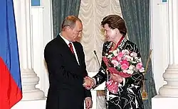 Un homme en costume avec un air grave serre la main d'une femme en tenue aux motifs de fleurs