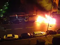 De nuit, une voiture en feu dans une rue.